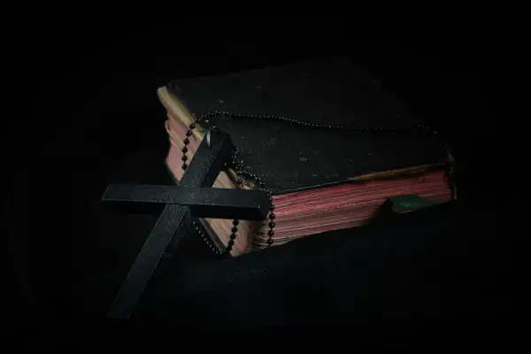 Czarny krzyż i paciorki różańca na starej księdze. Symbol wiary i modlitwa o spokój ducha w mroku.